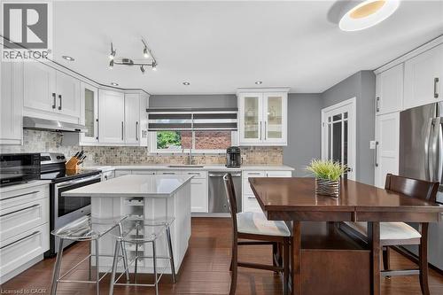 Kitchen featuring white shaker-style cabinetry, stainless steel appliances, a center island with countertop seating, a mosaic tile backsplash, and wood-finish flooring - 386 Upper Kenilworth Avenue, Hamilton, ON - Indoor