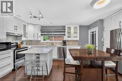 Kitchen featuring white shaker-style cabinetry, stainless steel appliances, a center island with countertop seating, a mosaic tile backsplash, and wood-finish flooring - 