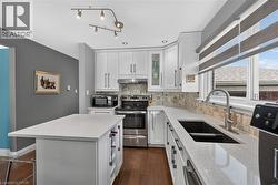 Modern kitchen featuring white cabinetry with brushed nickel hardware, light-toned countertops, wood-finish flooring, a mosaic tile backsplash, and recessed lighting - 