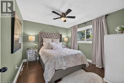 Wood-finish flooring with baseboard trim, wall-mounted ceiling fan, and a double-pane window - 