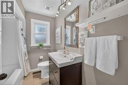 Bathroom featuring a white ceramic bathtub with shower, a single white vanity with an integrated sink and dark wood-finish cabinetry, and a white toilet - 