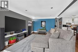 Open-concept living area featuring rich wood-finish flooring, recessed ceiling lighting, and a partial view of the kitchen with white cabinetry and stainless steel appliances - 