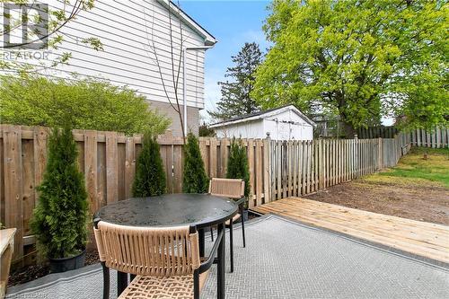 Private backyard featuring a patio area with a textured outdoor rug, a wooden deck extension, and a wooden privacy fence - 29 Woodlawn Avenue, Brantford, ON - Outdoor With Deck Patio Veranda