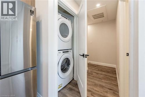 Dedicated laundry closet featuring a stackable washer and dryer, complemented by wood-finish flooring and a contemporary black door handle - 72 Erb Street E Unit# 103, Waterloo, ON - Indoor Photo Showing Laundry Room