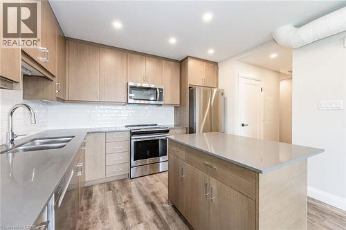 Modern kitchen featuring light wood-finish cabinetry, stainless steel appliances, a center island with a light-toned countertop, a subway tile backsplash, and wood-finish flooring - 72 Erb Street E Unit# 103, Waterloo, ON - Indoor Photo Showing Kitchen With Double Sink With Upgraded Kitchen
