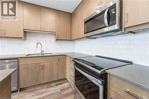 Modern kitchen featuring light wood-finish cabinetry, stainless steel appliances, white subway tile backsplash, gray countertops, and wood-finish flooring - 72 Erb Street E Unit# 103, Waterloo, ON - Indoor Photo Showing Kitchen With Double Sink
