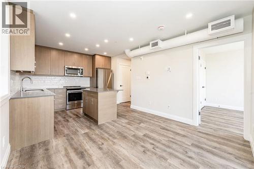 Modern kitchen featuring light wood-finish cabinetry, stainless steel appliances, a center island, and wood-finish flooring - 72 Erb Street E Unit# 103, Waterloo, ON - Indoor Photo Showing Kitchen