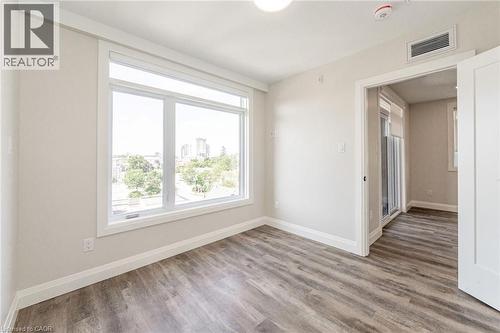 Bright interior space featuring a large window, wood-finish flooring, white baseboards, and a neutral wall color - 72 Erb Street E Unit# 103, Waterloo, ON - Indoor Photo Showing Other Room