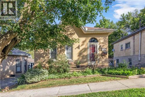 Light-toned brick exterior with an arched entry door and a covered front porch featuring wrought iron railing - 17 Scarfe Avenue, Brantford, ON - Outdoor