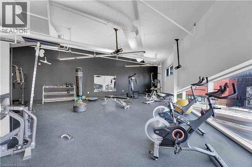 Fitness area featuring exposed ductwork, high ceilings, large windows, dark grey accent wall, and rubber flooring - 158 King Street N Unit# 81201, Waterloo, ON - Indoor Photo Showing Gym Room