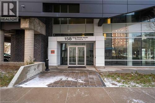 Modern building entrance featuring glass double doors, a white panel facade, dark brickwork, and concrete columns - 158 King Street N Unit# 81201, Waterloo, ON - Outdoor