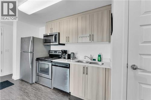 Kitchen featuring wood-finish cabinetry, stainless steel appliances, a double basin sink, light-toned countertops, and wood-finish flooring - 158 King Street N Unit# 81201, Waterloo, ON - Indoor Photo Showing Kitchen With Double Sink