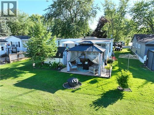 Expansive green lawn featuring a covered patio with a dark-roofed gazebo, a fire pit area with stone edging, and mature trees providing natural shading - 580 Beaver Creek Road Unit# 189, Waterloo, ON - Outdoor With Deck Patio Veranda