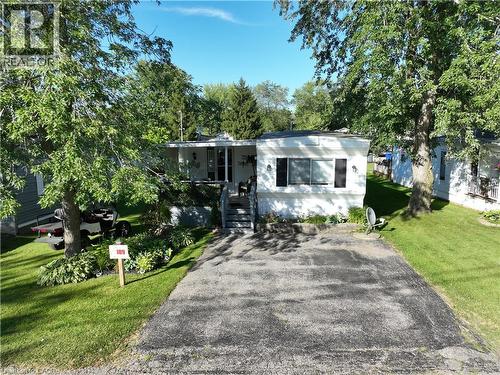 White exterior with dark contrasting shutters, front porch with railing, exterior lighting fixtures, mature trees, and a paved driveway - 580 Beaver Creek Road Unit# 189, Waterloo, ON - Outdoor