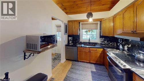 Kitchen featuring wood-finish cabinetry, black stone countertops, and a coordinating stone backsplash - 4101 Diana Park, Vineland, ON - Indoor Photo Showing Kitchen