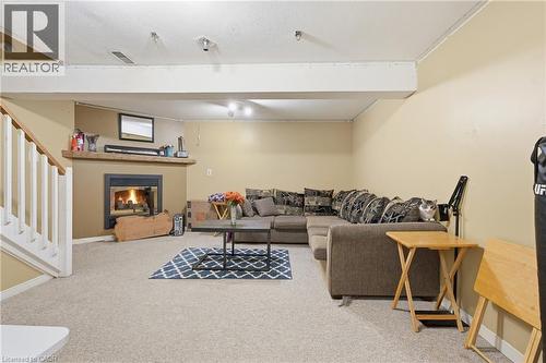 Carpeted lower-level room featuring a fireplace with a wood mantel, light beige walls, and a visible staircase with white balusters - 292 Mayview Court Unit# B, Waterloo, ON - Indoor With Fireplace