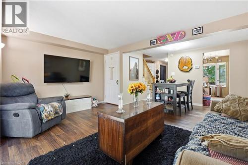 Open-concept living space featuring a wood-finish flooring throughout, wall-mounted flat-screen television, and a dark wood centerpiece table - 292 Mayview Court Unit# B, Waterloo, ON - Indoor Photo Showing Living Room
