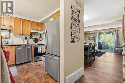 Open-concept kitchen and living area featuring stainless steel appliances, wood cabinetry, wood-finish flooring, and abundant natural light from multiple windows - 292 Mayview Court Unit# B, Waterloo, ON - Indoor Photo Showing Kitchen