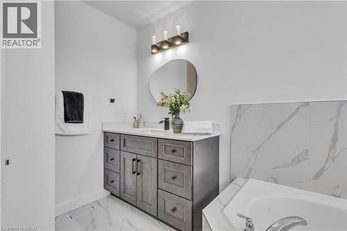 Bathroom featuring a wood-finish vanity with a light-colored countertop, an irregular shaped mirror, and overhead vanity lighting - 73 Fitzgerald Drive, Cambridge, ON - Indoor Photo Showing Bathroom