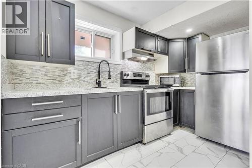 Modern kitchen featuring dark cabinetry with brushed nickel hardware, white stone-finish countertops, and a mosaic tile backsplash - 73 Fitzgerald Drive, Cambridge, ON - Indoor Photo Showing Kitchen With Upgraded Kitchen