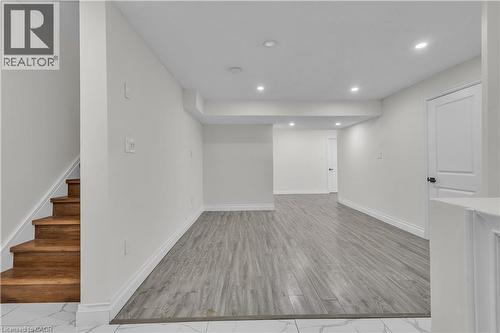 Spacious lower-level area featuring recessed lighting, wood-finish flooring, white baseboards, and a bright white door with dark hardware - 73 Fitzgerald Drive, Cambridge, ON - Indoor Photo Showing Other Room