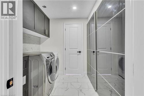 Laundry area featuring a tile backsplash, dark cabinetry, and white flooring - 73 Fitzgerald Drive, Cambridge, ON - Indoor Photo Showing Laundry Room