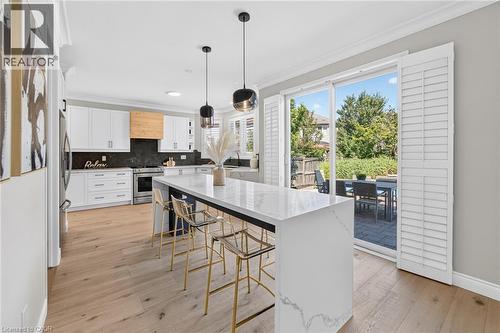 Bright kitchen featuring light wood-finish flooring, white cabinetry, dark stone backsplash, and a large central island with a light-colored countertop - 1533 Morse Place, Milton, ON - Indoor Photo Showing Kitchen With Upgraded Kitchen