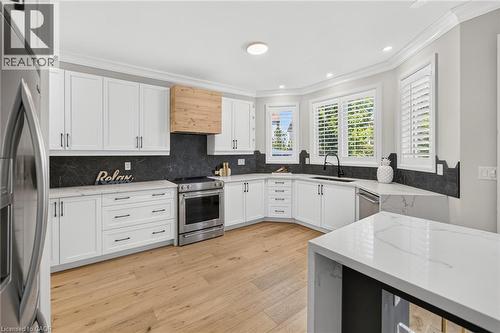 Modern kitchen featuring white shaker cabinetry, stainless steel appliances, a wood-finish range hood, and light wood-finish flooring - 1533 Morse Place, Milton, ON - Indoor Photo Showing Kitchen
