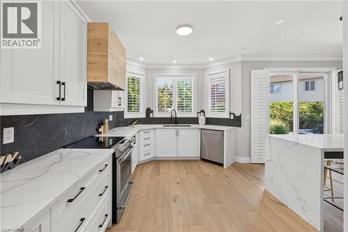 Modern kitchen featuring white shaker cabinetry, stainless steel appliances, a wood-finish range hood, black hexagonal tile backsplash, and light wood-finish flooring - 1533 Morse Place, Milton, ON - Indoor Photo Showing Kitchen With Upgraded Kitchen