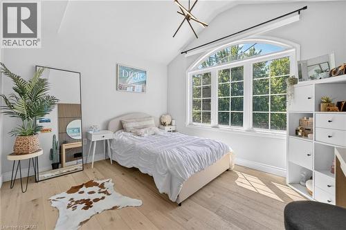 Bright room featuring a large arched window, vaulted ceiling, wood-finish flooring, and a contemporary linear chandelier - 1533 Morse Place, Milton, ON - Indoor Photo Showing Bedroom