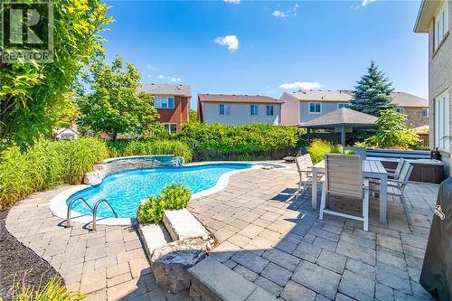 Outdoor entertaining space featuring a freeform swimming pool with a waterfall feature, a spacious paver patio, a built-in hot tub, and a covered gazebo - 1533 Morse Place, Milton, ON - Outdoor With In Ground Pool With Deck Patio Veranda