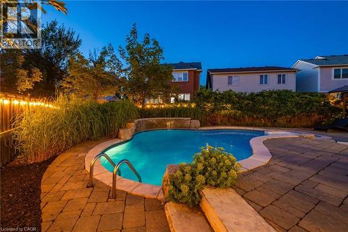 Curved inground pool featuring a waterfall, stone coping, and integrated lighting - 1533 Morse Place, Milton, ON - Outdoor With In Ground Pool With Backyard