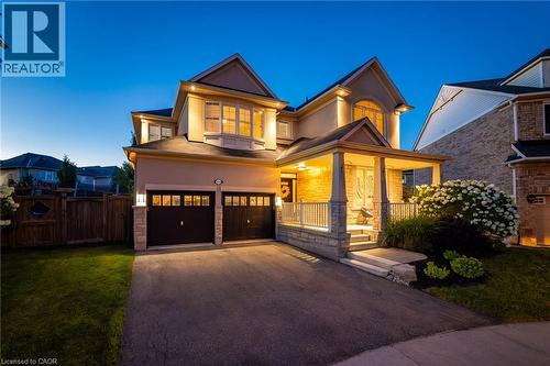 Exterior featuring a stone and stucco facade, a covered front porch with stone pillars, a two-car garage with carriage-style doors, a paved driveway, and mature landscaping - 1533 Morse Place, Milton, ON - Outdoor