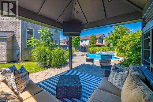 Covered outdoor living space featuring a vaulted ceiling with integrated ceiling fans, striped area rug, built-in seating with cushions, and direct sightlines to the resort-style pool and mature lands - 1533 Morse Place, Milton, ON - Outdoor With In Ground Pool With Deck Patio Veranda