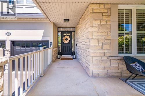 Inviting covered front entrance featuring a dark paneled door with glass inserts, stone façade accents, a concrete walkway, white railings, and a two-car garage - 1533 Morse Place, Milton, ON - Outdoor With Exterior