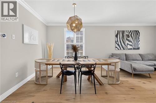 Open-concept living area featuring light wood-finish flooring, crisp white crown molding, and a modern geometric pendant light fixture - 1533 Morse Place, Milton, ON - Indoor Photo Showing Other Room