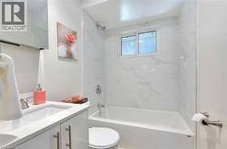 Bathroom featuring a white vanity with an undermount sink, a coordinating white countertop, and a built-in bathtub with a shower - 