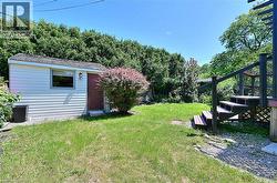 Expansive backyard featuring a storage shed with siding exterior, mature perimeter trees, a dark-stained deck with stairs, and a gravel area - 