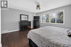 Spacious room featuring wood-finish flooring, light grey walls, and a multi-pane window framing exterior trees - 