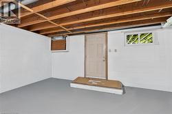 Unfinished basement space featuring exposed wood joists, painted block walls, and a painted concrete floor - 