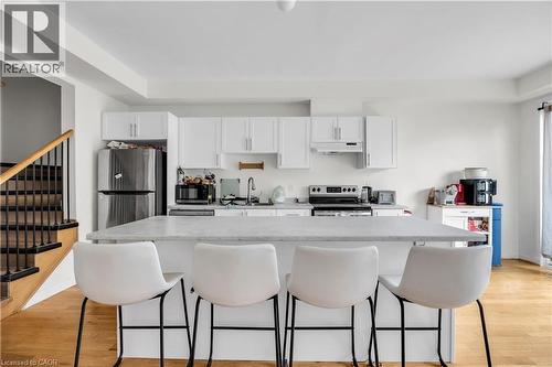 Kitchen featuring a central island with countertop seating, white cabinetry, stainless steel appliances, and wood-finish flooring - 1451 Green Road, Bowmanville, ON - Indoor Photo Showing Kitchen