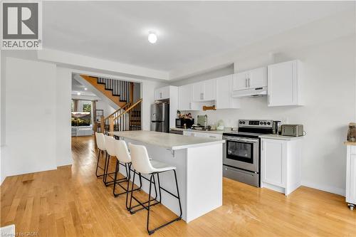 Kitchen featuring white cabinetry, stainless steel appliances, a center island with countertop seating, and wood-finish flooring - 1451 Green Road, Bowmanville, ON - Indoor Photo Showing Kitchen