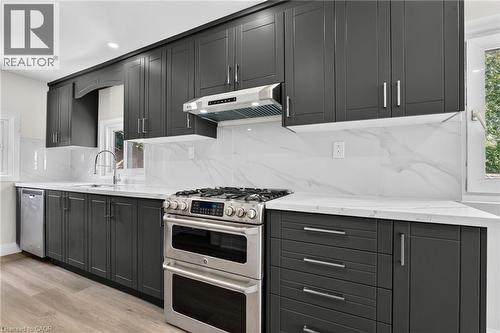 Modern kitchen featuring dark cabinetry, white countertops, a stainless steel range with a double oven, a matching range hood, and a white tile backsplash - 36 Mahony Avenue, Hamilton, ON - Indoor Photo Showing Kitchen With Upgraded Kitchen
