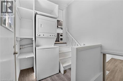 Laundry area with a stacked washer and dryer, built-in shelving, wood-finish flooring, and white painted walls - 36 Mahony Avenue, Hamilton, ON - Indoor Photo Showing Laundry Room