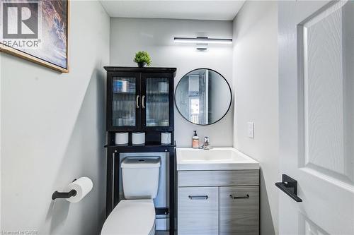Bathroom featuring a single vanity with integrated sink, wood-finish cabinetry, a round wall-mounted mirror, and a wall-mounted linear light fixture - 233 Red Clover Court, Kitchener, ON - Indoor Photo Showing Bathroom