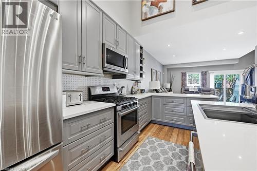 Open-concept kitchen featuring light gray cabinetry, white countertops, stainless steel appliances, and wood-finish flooring - 10 Kopperfield Lane, Hamilton, ON - Indoor Photo Showing Kitchen With Upgraded Kitchen
