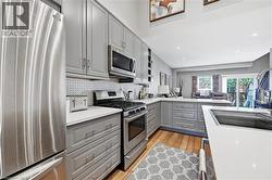 Open-concept kitchen featuring light gray cabinetry, white countertops, stainless steel appliances, and wood-finish flooring - 