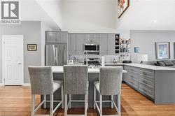 Open-concept kitchen featuring an island with seating, grey cabinetry, stainless steel appliances, and wood-finish flooring - 