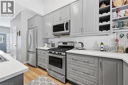 Kitchen featuring light gray cabinetry with brushed nickel hardware, stainless steel appliances, solid surface countertops, a white pegboard backsplash, and wood-finish flooring - 