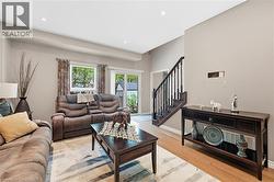 Open living space featuring wood-finish flooring, recessed lighting, and a prominent staircase with dark wood railings - 